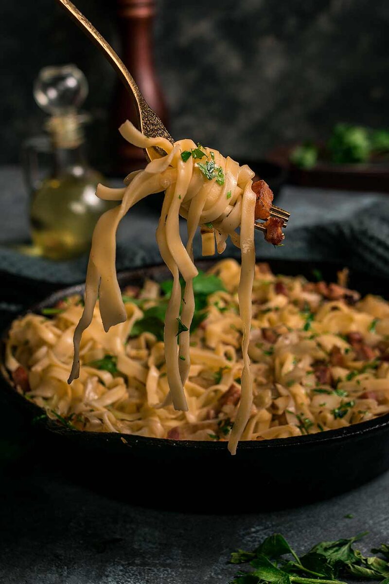 Creamy tagliatelle carbonara lifted on a fork over a cast-iron pan