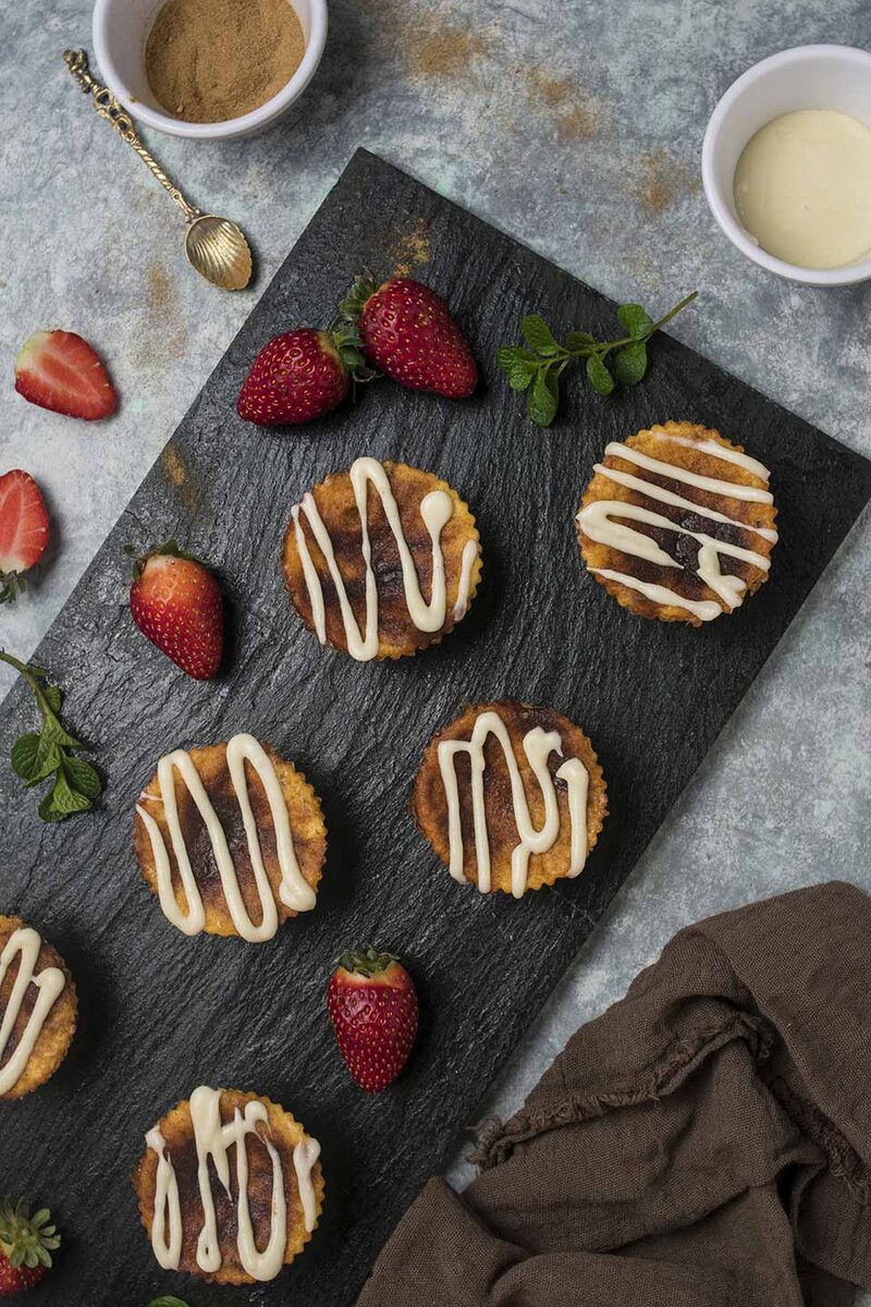 Mini cinnamon roll cheesecakes drizzled with icing on slate, overhead