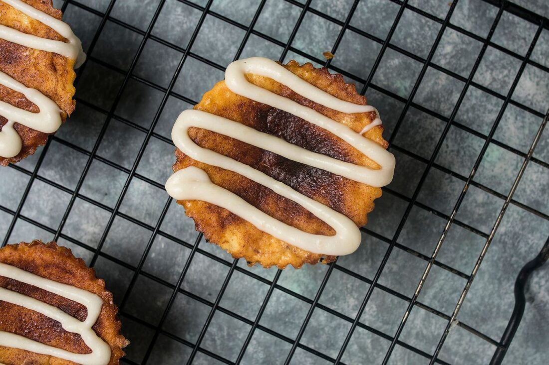 Baked cheesecakes with icing drizzle on a cooling rack
