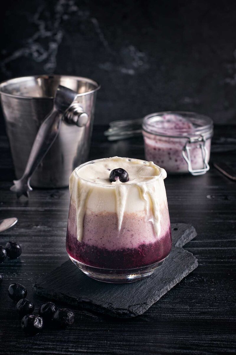 Layered blueberry smoothie in a glass on dark wood